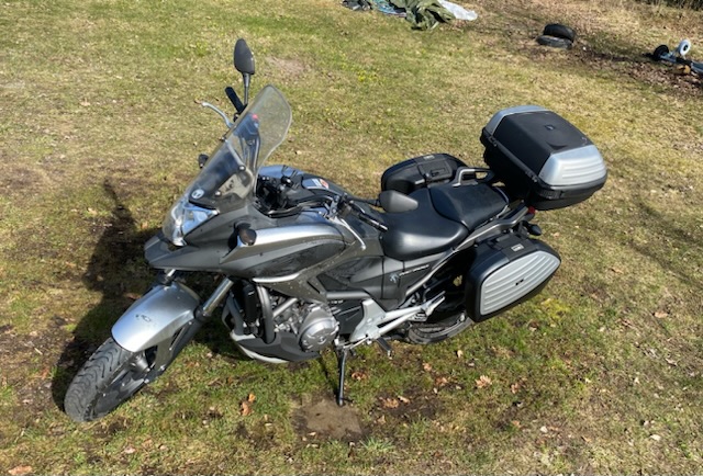Black and silver motorcycle standing on grass, glowing in the sun. The Honda NC700X.